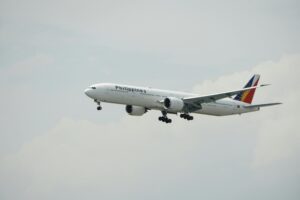 A Philippine Airlines Boeing 777 aircraft flying against a cloudy sky.